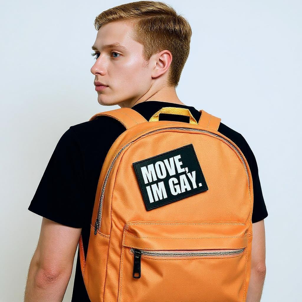Person wearing an orange backpack with a 'MOVE, IM GAY.' patch on a plain background