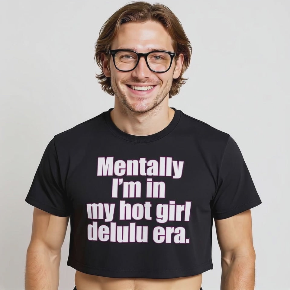 Smiling model in a black crop top with bold pink and white text that says, “Mentally I’m in my hot girl delulu era,” highlighting queer humor, gender-inclusive streetwear, and viral TikTok fashion culture.