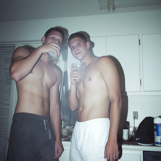 Two shirtless young men hanging out in a kitchen, casually sipping drinks, showing off confident queer energy and relaxed masculine style—capturing the vibe that inspires The Bayou WeHo’s LGBTQ+ apparel and gay fashion aesthetic.