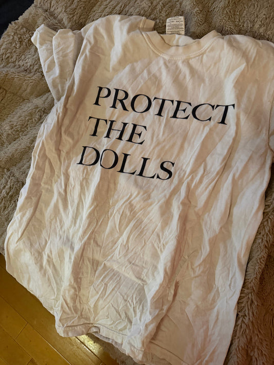 Protect the dolls tee supporting trans rights on sale for 30% off. All proceeds go to trans lifeline. on a bed.