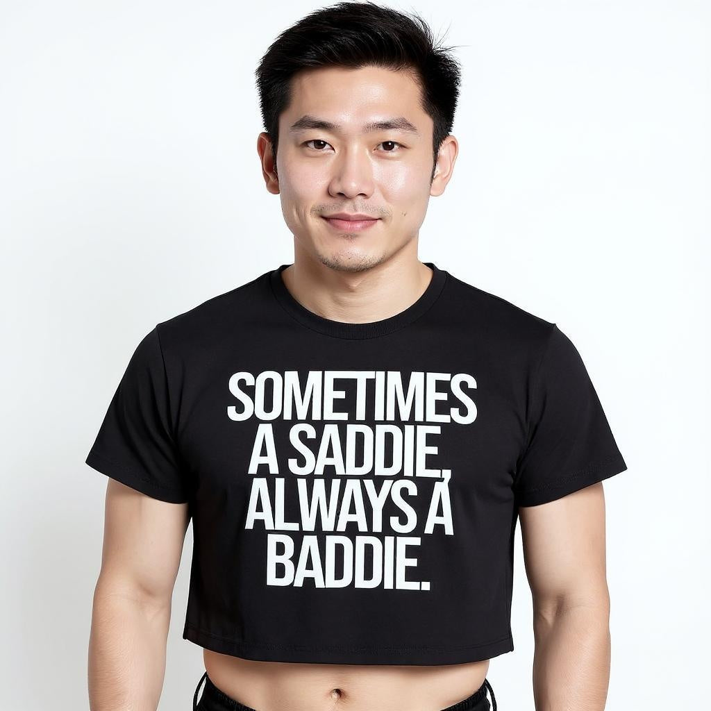 Man wearing a black t-shirt with white text saying "Sometimes A Saddie, Always A Baddie" on a plain background