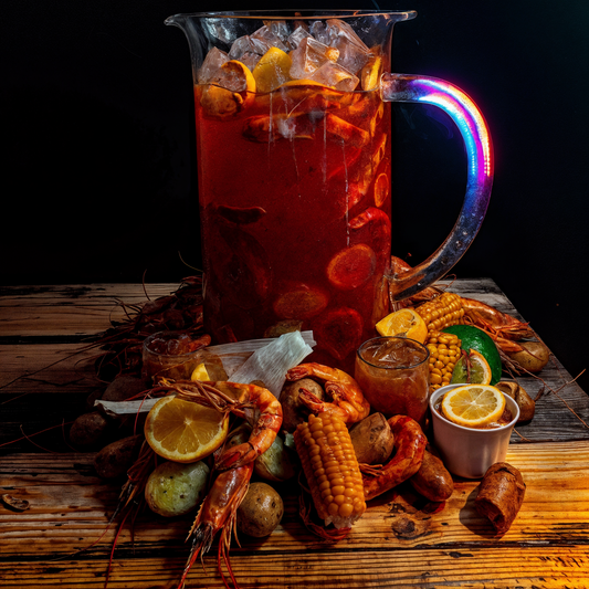 Pitcher of cocktail in West Hollywood with a colorful handle, surrounded by a Cajun seafood boil and vegetables on a wooden surface at bayou weho.