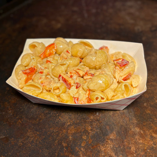 Macaroni, Lobster, and cheese with red peppers in a paper container on a dark surface
