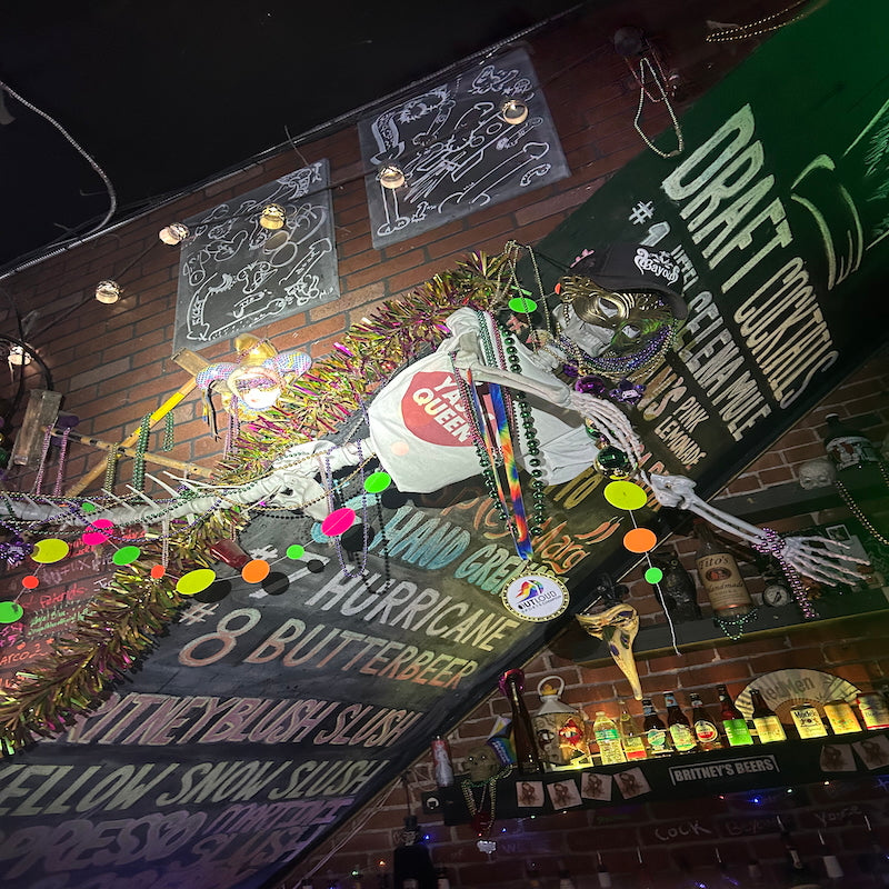 Decorative skeleton with colorful lights on a bar counter, featuring signs and a 'Butterbeer' sign.