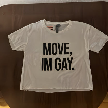 White t-shirt with 'MOVE, IM GAY.' text on a brown surface