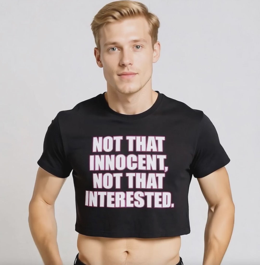 Man wearing a Britney Spears-inspired crop top that is black with white writing and pink outlining "NOT THAT INNOCENT, NOT THAT INTERESTED" for LGBTQIA+ merch