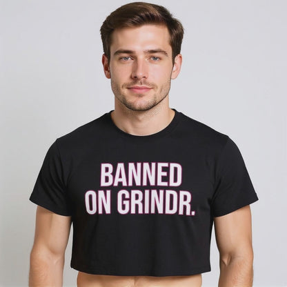 The model is wearing a black crop top with bold pink and white text reading “BANNED ON GRINDR,” showcasing queer humor, LGBTQ+ streetwear, and gender-inclusive viral fashion.