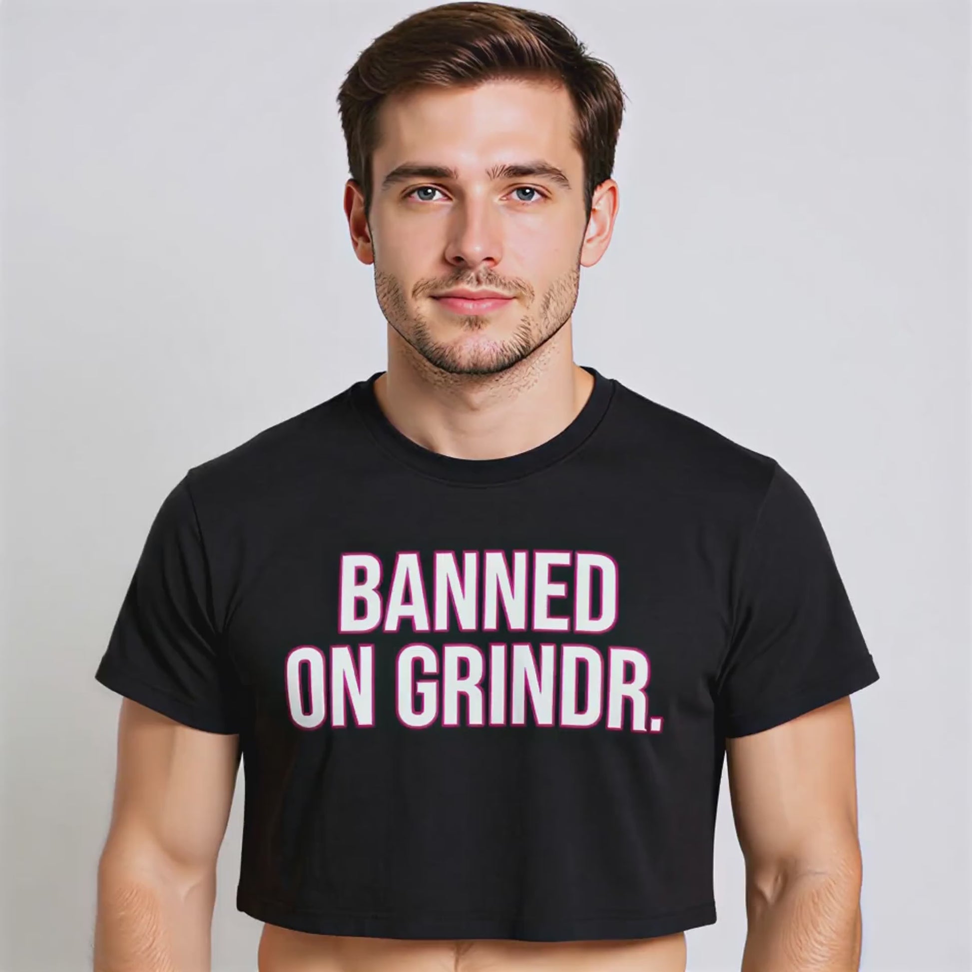 A male model wearing a black crop top with the words "Banned On Grindr" in white lettering with a pink outline on the front.