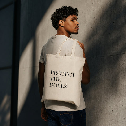 Man holding a tote bag with 'PROTECT THE DOLLS' text against a concrete wall.