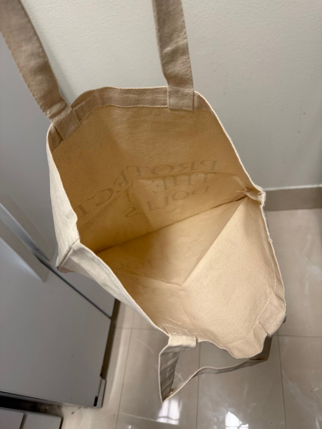 Beige tote bag with text on a tiled floor